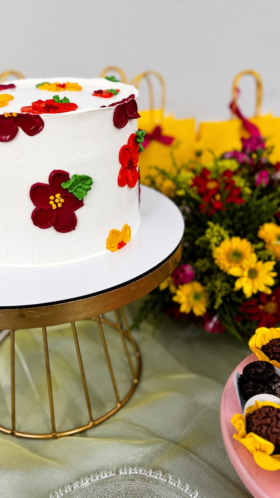 Bolo branco decorado com flores vermelhas e amarelas em mesa de festa