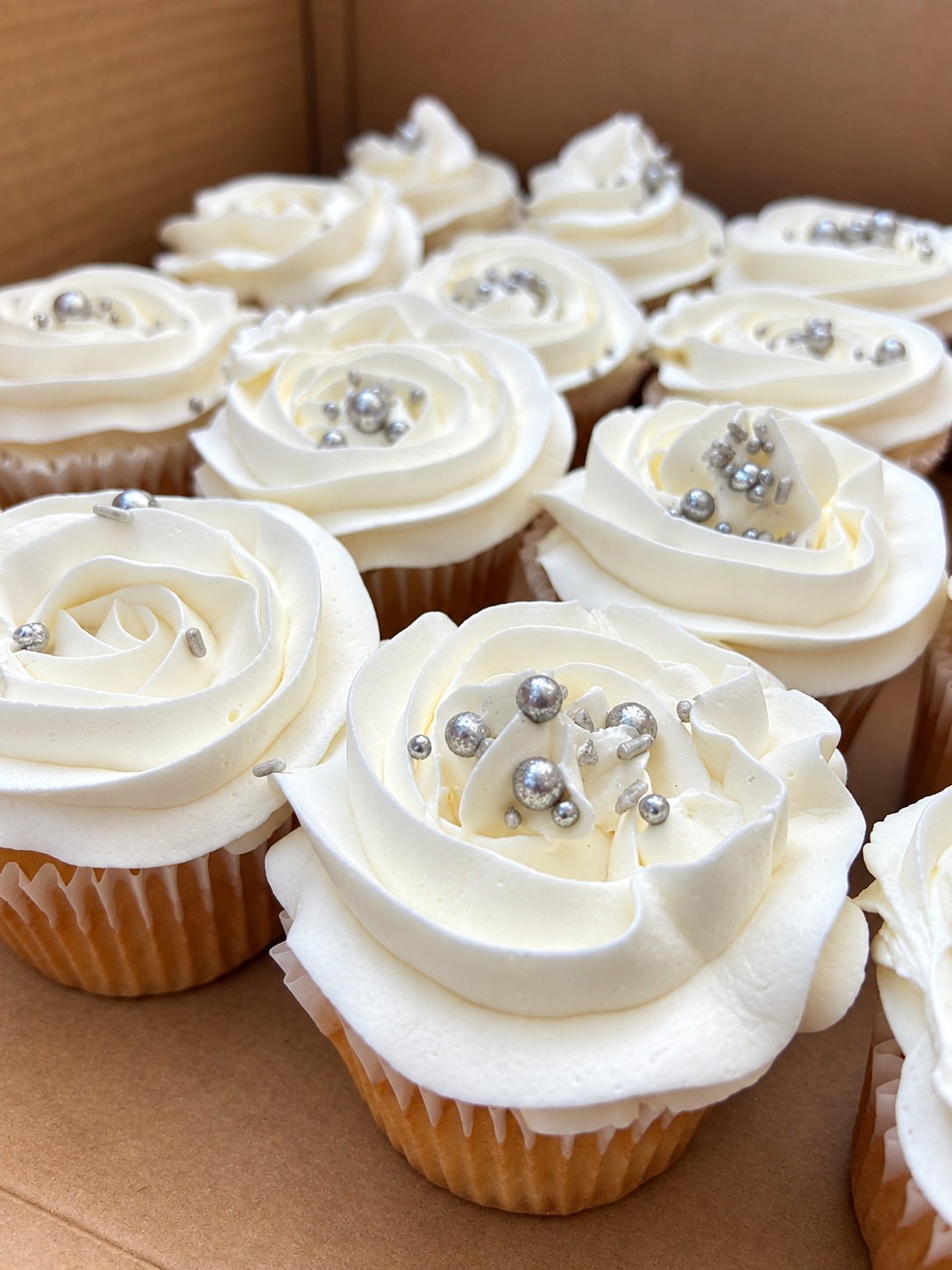 Cupcakes com delicadas rosas de creme branco e confeitos prateados